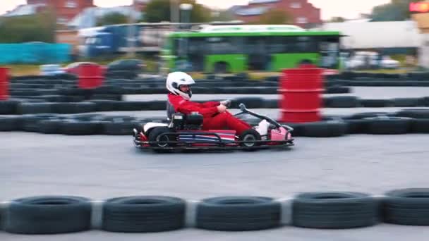 Primo piano dei piloti di kart in uniforme protettiva che si muovono sul kart rosso vicino alle barriere di sicurezza fatte di vecchie ruote sulla pista di kart all'aperto. media. Allenamento di guida kart. Kart racing — Video Stock