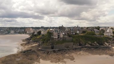 Yazın gri bulutlu gökyüzüne karşı kumlu nehir kenarındaki gri Avrupa şehrinin güzel hava manzarası. Başla. Muhteşem Avrupa mimarisi