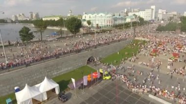 Sıcak bir yaz günü, mavi bulutlu gökyüzüne karşı geniş nehrin kenarındaki sette yürüyen bir sürü insanın hava manzarası. Başla. Büyük şehrin yaz hayatı