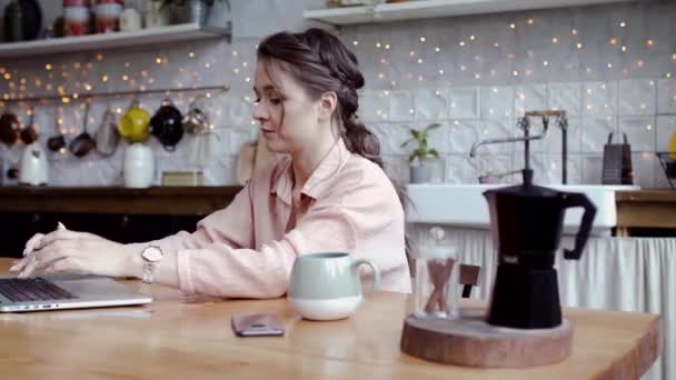 Jeune femme attrayante travaillant sur ordinateur portable à la maison dans la cuisine. Images d'archives. Belle femme travaillant soigneusement sur ordinateur portable en mode freelance et fond de cuisine confortable — Video