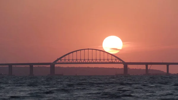 Потрясающий вид на красивый закат над большой рекой и мостом, эффект временной давности. Выстрел. Яркое золотое солнце движется к горизонту над рекой . — стоковое фото