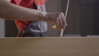 Üstü örtülü bir işçinin, arka plandaki ahşap deliğin içindeki fırçayla yapıştırıcı sürmesini yakın çekim. Başla. Erkek marangoz odunla çalışıyor..