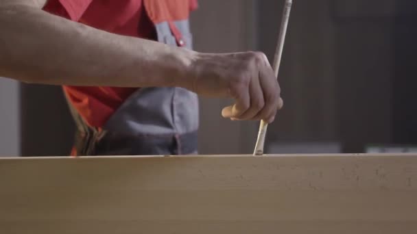 Close-up van een werkman in coverall aanbrengen lijm met een borstel in het gat van een houten balk op wazige achtergrond. Actie. Mannelijke timmerman werkend met hout. — Stockvideo