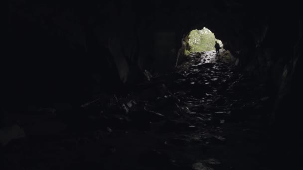 Sylwetka odkrywcy jaskiń w podziemiu z wejściem za nim, koncepcja turystyki i przyrody. Materiał filmowy. mężczyzna turysta chodzenie wewnątrz jaskini. — Wideo stockowe