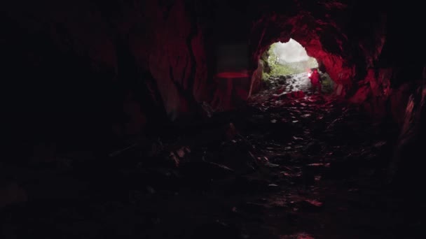 Человек спускается в пещеру, оставляя за собой вход, крайняя и спортивная концепция. Запись. Турист в подземной пещере с красной сигнальной ракетой . — стоковое видео