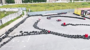 Güneşli bir günde eski siyah araba lastikleriyle hipodromda ilerleyen koruyucu üniformalı ve kasklı araba yarışçılarının hava görüntüsü. Medya. Karting Şampiyonası