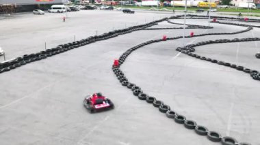 Koruyucu kırmızı üniformalı ve kasklı Kart yarışçıları eski siyah araba lastikleriyle pistte ilerliyorlar. Medya. Kart sürüş eğitimi.