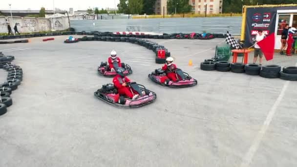 Primo piano dei piloti in uniforme protettiva rossa e casco che iniziano a muoversi dalla linea di partenza sui kart rossi. I media. Allenamento di guida kart. Kart racing — Video Stock