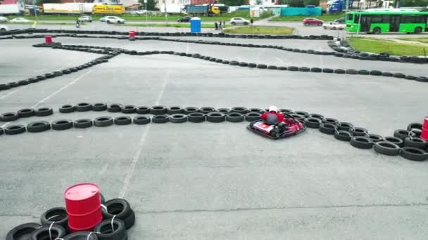 Vista de cerca del corredor de karts en uniforme rojo protector y casco blanco tratando de arreglar su kart cerca de los viejos neumáticos de automóviles negros. Medios. Formación de conducción de karts . — Vídeos de Stock