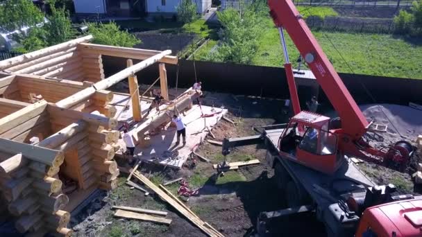 Werknemers met kraanlift houten structuur van huis. Een knip. Bovenaanzicht van het proces van het installeren van gevel van houten dak met behulp van werknemers en kraan — Stockvideo