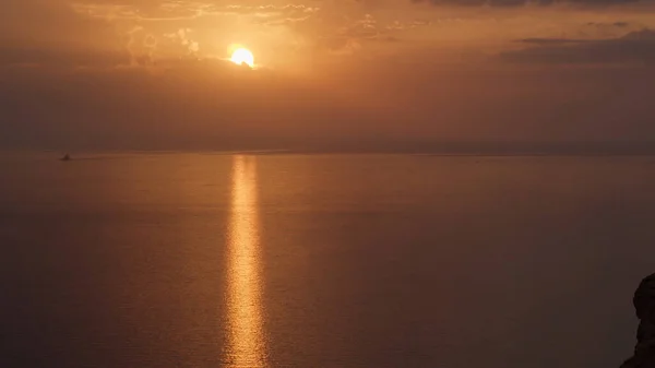 Breathtaking sunset over the Atlantic ocean with the bright golden sun coming down to the horizon. Shot. Aerial of the calm ocean, black cliff, and bronze sunset. — Stock Photo, Image