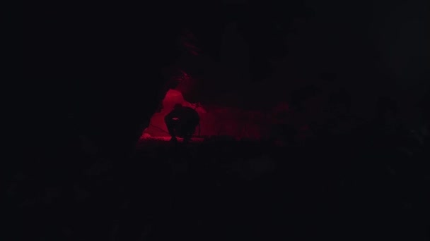 男不法占拠の背面ビューと地下の洞窟の穴の中を見て。ストック映像だトーチの代わりに赤い燃焼信号フレアを使用するエクスプローラ. — ストック動画