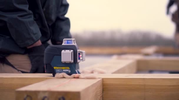 Gros plan du travailleur nivellement poutre en bois sur le chantier de construction sur fond de ciel nuageux brillant. Clip. Constructeurs masculins faisant le cadre en bois de la maison . — Video