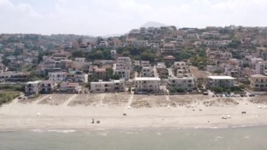 Açık mavi deniz suyu ve deniz kıyısındaki küçük yazlık otellerin ılık yaz gününde mavi bulutlu gökyüzüne karşı hava manzarası. Başla. Muhteşem yaz tatili
