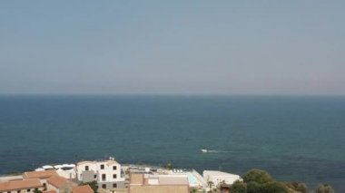 Açık mavi deniz suyu ve deniz kıyısındaki küçük yazlık otellerin ılık yaz gününde mavi bulutlu gökyüzüne karşı hava manzarası. Başla. Muhteşem yaz tatili