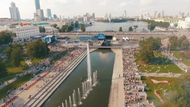 Повітряний вид великої кількості людей йде по набережній з фонтанами біля річки в теплий літній день проти блакитного хмарного неба. Почали. Літо у великому місті. — стокове відео