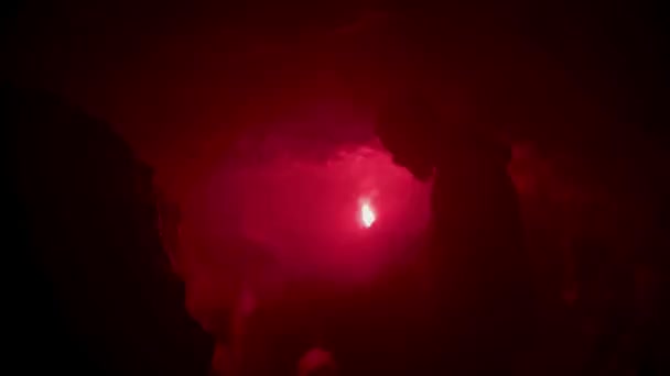Молодой человек обнаружил в пещере узкую дыру и осветил путь красной сигнальной ракетой. Запись. Абсолютно глубокая тьма вокруг грота . — стоковое видео