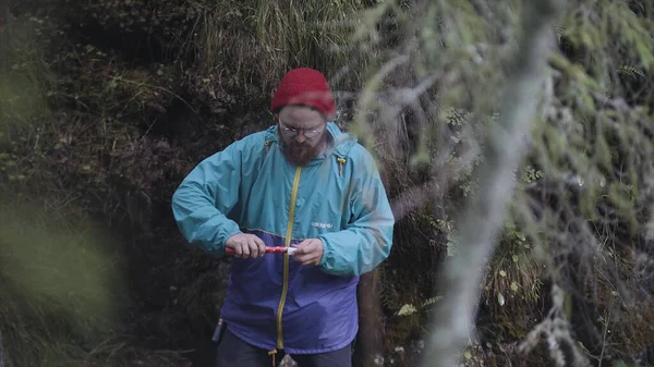 Young man holds up red smoke flare to signal for help in the middle of green wild nature. Stock footage. Hipster traveler lost in the forest and asking for help, SOS.