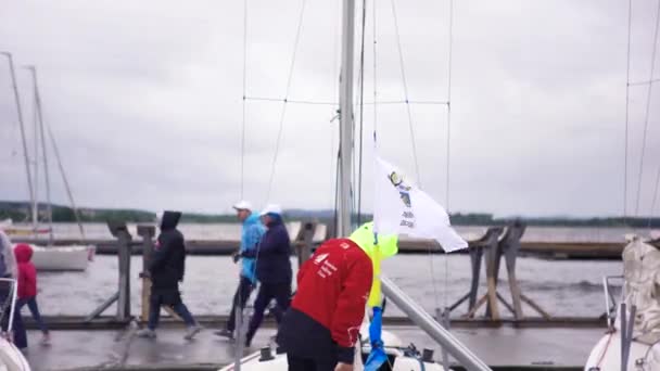 Homme debout dans un bateau à moteur amarré près du pont avec des gens le traversant sur fond gris ciel nuageux. L'art. Groupe de personnes marchant près du yacht . — Video