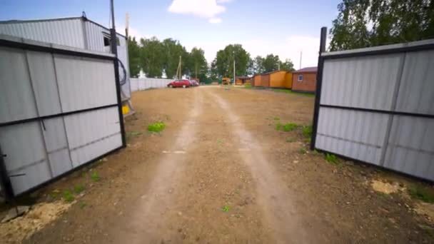 Durch das Tor zum Bauernhof mit Waldgipfeln und blauem Himmel. Kunst. kleine Holzhäuser auf dem Land. — Stockvideo