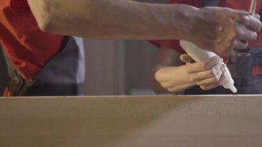 Yapıştırıcıyı yapıştırıcı yüzeylere yayan iki erkek kapariye yaklaşın. Başla. İşçi elleri ahşap kirişe yapıştırıcı sürüyor.
