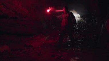 Adam yanan bir işaret fişeğiyle karanlık mağaranın içinde yolunu aydınlatıyor ve girişi arkasında bırakıyor. Stok görüntüleri. Karanlık mağaranın içinde tehlikeli turizm.