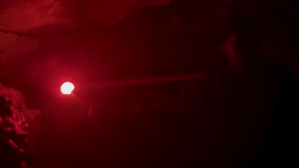 Young man found a narrow hole inside the cave and illuminates the way with red burning signal flare. Stock footage. Absolutely deep darkness around in grotto. — Stock Video