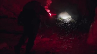 Kırmızı işaret fişeği olan bir adam mağaradan çıkmak için ışığa doğru gidiyor. Stok görüntüleri. Başarı kavramı, karanlık bir mağaranın çıkışındaki adam..