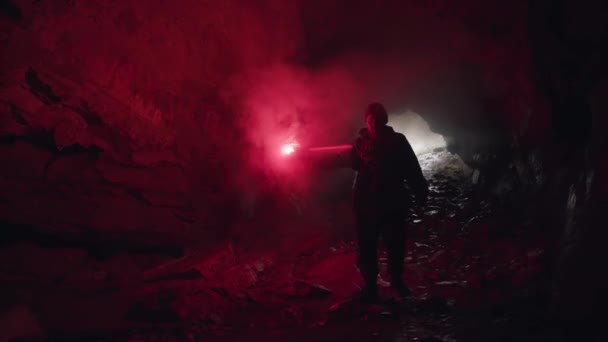 Een man die zich een weg baant in een donkere grot met een brandende signaalvlam en de ingang achter zich laat. Voorraadbeelden. Gevaarlijk toerisme in donkere grot. — Stockvideo