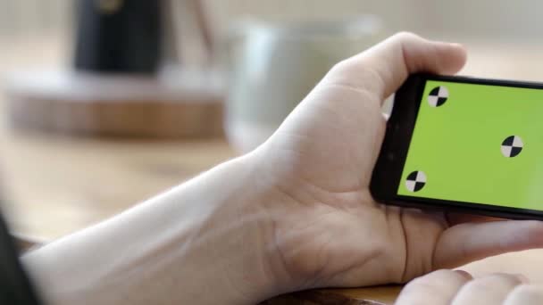 Крупним планом рука тримає телефон горизонтально з зеленим екраном. Стокові кадри. Людина тримає телефон горизонтально однією рукою для перегляду відео або фільмів — стокове відео