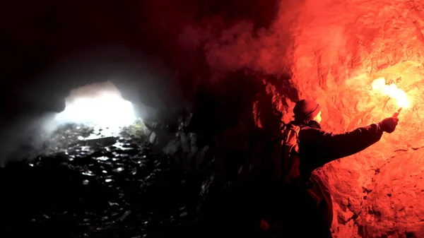 Hombre solitario con una llamarada de señal roja en una caverna oscura buscando el agujero, el concepto de turismo. Imágenes de archivo. Hombre explorando cueva subterránea . — Foto de Stock