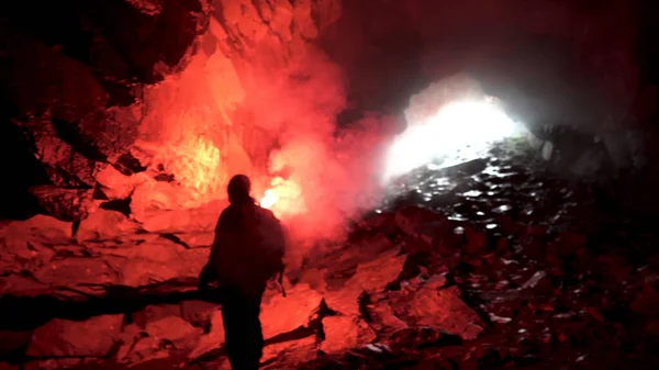Eenzame man met een rood brandend signaal in een donkere grot op zoek naar het gat, toeristisch concept. Voorraadbeelden. Mannelijke verkennen ondergrondse grot. — Stockfoto