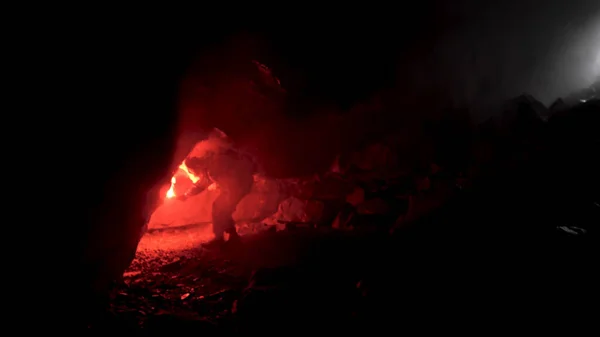 Man geologist with a red burning signal flare exploring underground dark cave, science concept. Stock footage. Scientist trying to find a way out of the cave.