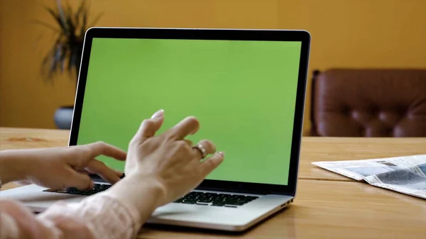 Green laptop screen and female hands typing. Stock footage. Elegant hands of woman typing on laptop with green screen. Close-up of woman working on laptop typing articles