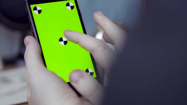Man met mobiele smartphone thuis. Voorraadbeelden. Close-up van een telefoon met een groen scherm in de handen van een man — Stockvideo
