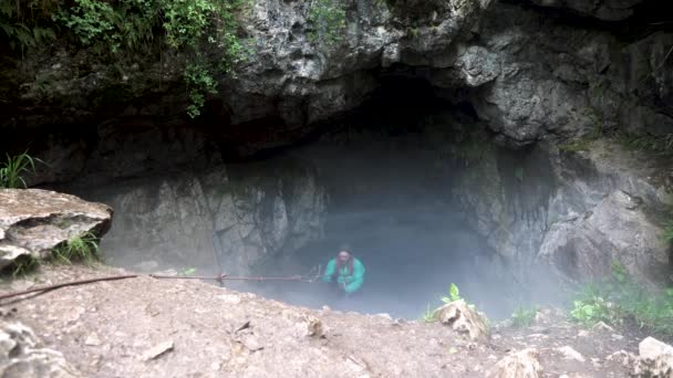 Homem tentando sair da caverna nebulosa com as mãos segurando corda, conceito de trekking perigoso. Imagens de stock. Explorador usando a corda de escalada para sair da caverna . — Vídeo de Stock