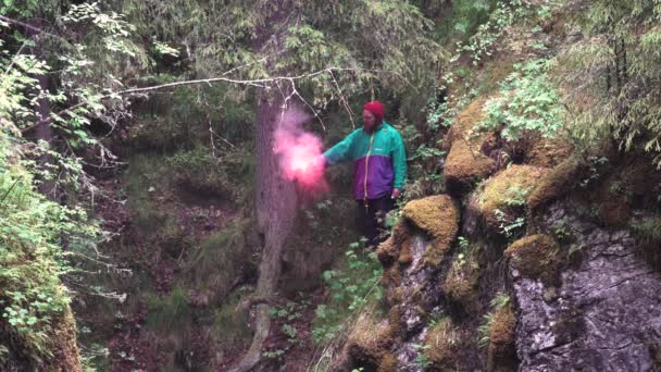 Wandelaar in heldere kleren observeren de groene planten van de klif en houden een brandende rode signaal vlam. Voorraadbeelden. Explorer verloren in het bos, Sos concept. — Stockvideo