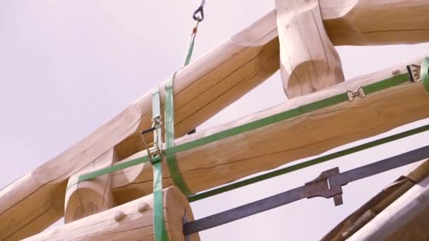 Vista inferior de la construcción de una casa ecológica de madera. Clip. La parte del techo de la casa inacabada del tronco colgando de eslingas de construcción . — Vídeos de Stock