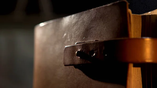 Old leather book with a strap. Stock footage. Close up of an ancient leather brown diary or book with yellow pages isolated on black background.