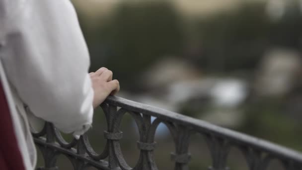 Vista trasera de una mujer vestida de blanco en el balcón. Imágenes de archivo. El primer plano de la mano tierna de una hembra tocando pasamanos de hierro del balcón sobre fondo borroso . — Vídeo de stock