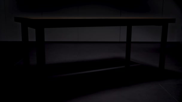 Dřevěný stůl na černém pozadí. Záběry ze skladu. Zavřít dřevěný stůl s černými železnými nohami stojící v prázdné místnosti ve tmě, která se mění podle světla. — Stock video