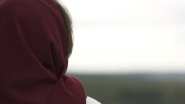Yeşil ormanın, tarlanın ve nehrin üzerinde duran bir kadının dikiz görüntüsü. Stok görüntüleri. Kafasında kırmızı eşarp ve beyaz ceket olan dişiden doğal yay ya da