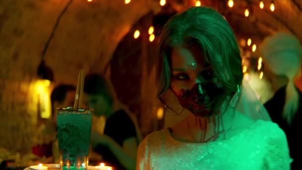 Jonge vrouw met enge make-up met een drankje en kaarsen. Voorraadbeelden. Een meisje serveerster met een griezelig gezicht van een zombie tijdens Halloween feest in de nachtclub. — Stockvideo