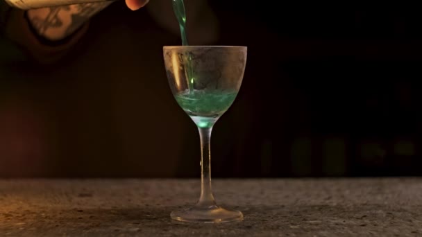 Vinglas med grön cocktail på svart bakgrund. Lagerbilder. Närbild av en hand hälla alkoholhaltig dryck av grön färg med lysande partiklar. — Stockvideo