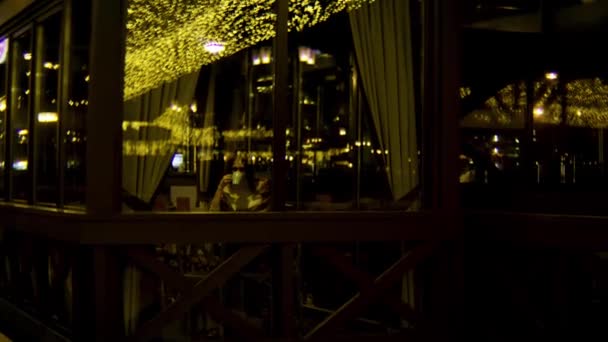 Beautiful girl in a cafe sitting and drinking tea. Stock footage. Young woman drinks coffee in cafe in the cold weather, view behind the window glass. — Stock Video