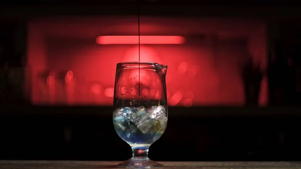 Frisches alkoholisches Getränk mit Eiswürfeln auf der Theke ins Glas gießen. Archivmaterial. Nahaufnahme des Prozesses der Cocktailzubereitung, indem blauer Sirup ins Glas gegeben wird. — Stockfoto