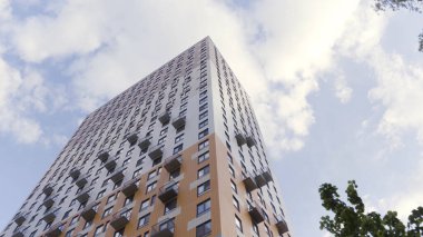 Mavi bulutlu arka planda bir apartmanın alt manzarası. Stok görüntüleri. Yakında bir sürü dairesi ve yeşil ağaçları olan yeni bir ev..