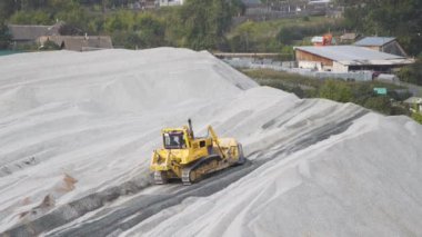 Buldozer taş ocağına moloz saçıyor. Stok görüntüleri. Sarı inşaat traktörü taş ocağında çalışıyor ve köyün yakınına çakıl yayıyor..