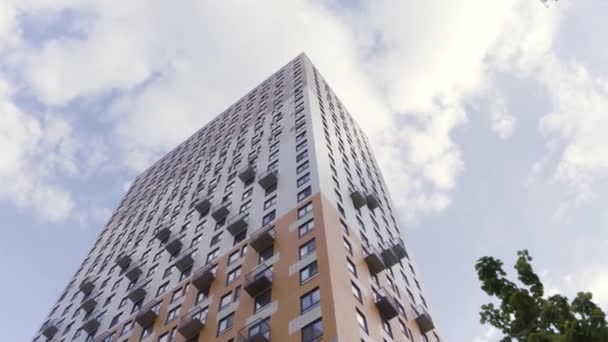 Blick von unten auf ein Mehrfamilienhaus auf blauem bewölkten Himmel Hintergrund. Archivmaterial. Neues Wohnhaus mit vielen Wohnungen und grünen Bäumen in der Nähe. — Stockvideo