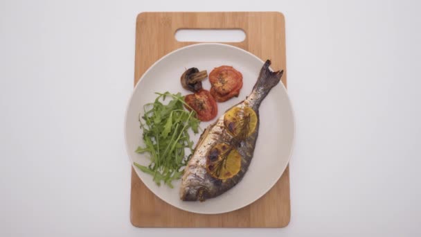 Baked fish with lemon and spices in restaurant. Action. Beautifully served fish in restaurant on white background. Simple elegant serving of baked fish on white plate — Stock Video